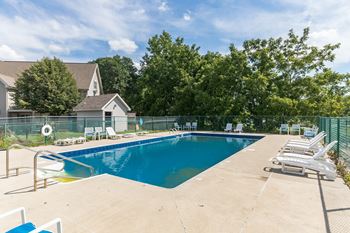 A large swimming pool surrounded by a concrete deck and lounge chairs.