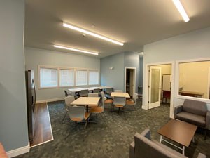 A room with grey carpet and white walls has a long table with chairs around it.