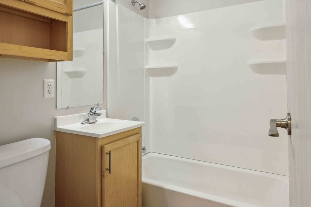 A white sink with a wooden cabinet and a white bathtub with a glass shower door.