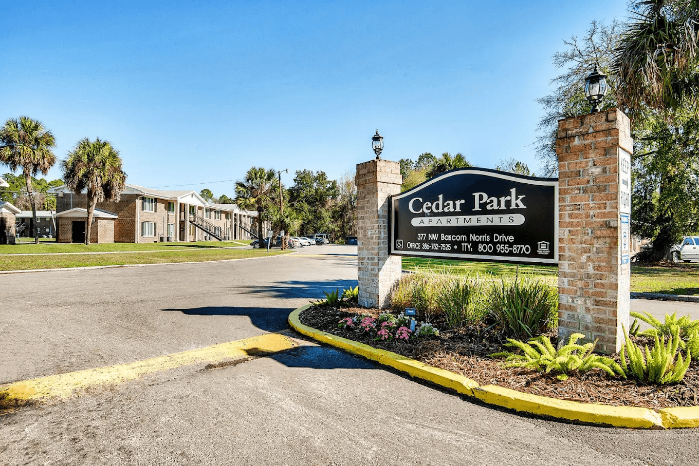 The image shows a sign for Cedar Park Apartments with a parking lot in the foreground.