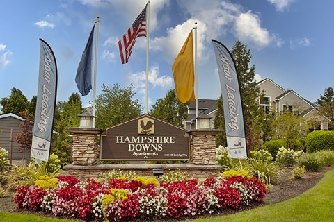 Hampshire Downs Apartments sign with flags and flowers in front.