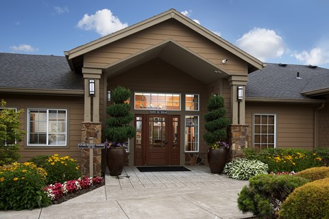 A building with a brown door and windows surrounded by plants.