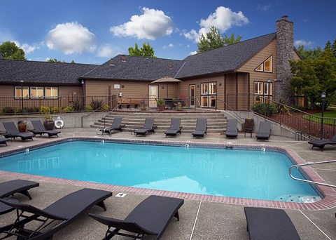 A large outdoor swimming pool surrounded by lounge chairs and a building in the background.