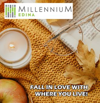 a candle in a jar sitting on top of a sweater with a book and autumn leaves