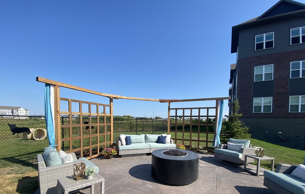 a patio with a firepit and a wooden pergola with blue curtains