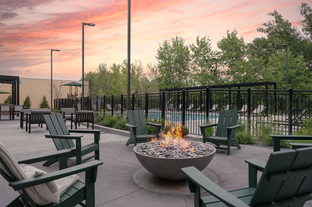 an outdoor patio with a fire pit and chairs at sunset