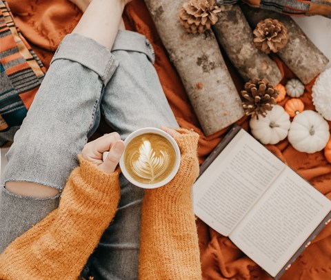A person in a yellow sweater is holding a cup of coffee with a latte art design on it.
