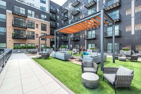 an outdoor lounge area with couches and tables in front of an apartment building