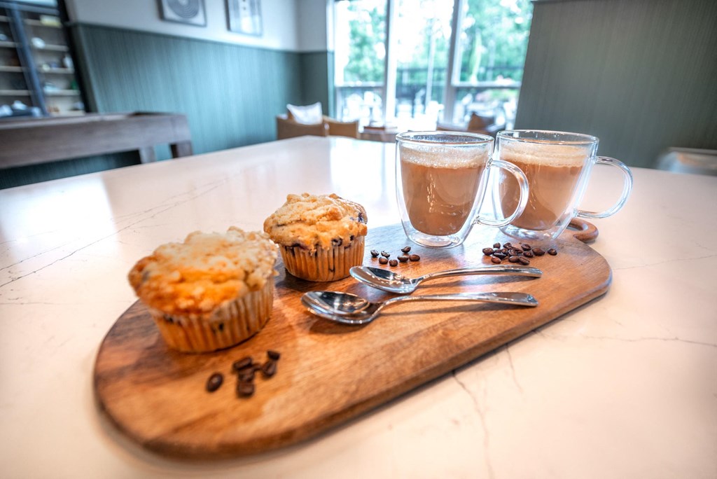 a wooden cutting board with muffins and two cups of coffee
