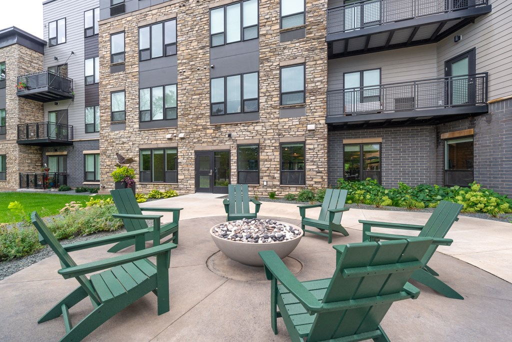 an outdoor patio with chairs and a fire pit in front of an apartment building