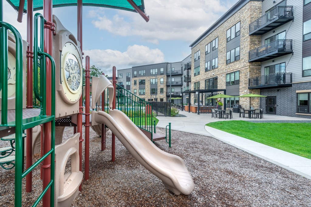 a playground with a slide and other playground equipment with apartments in the background