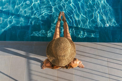 A woman in a straw hat is sitting on the edge of a pool.