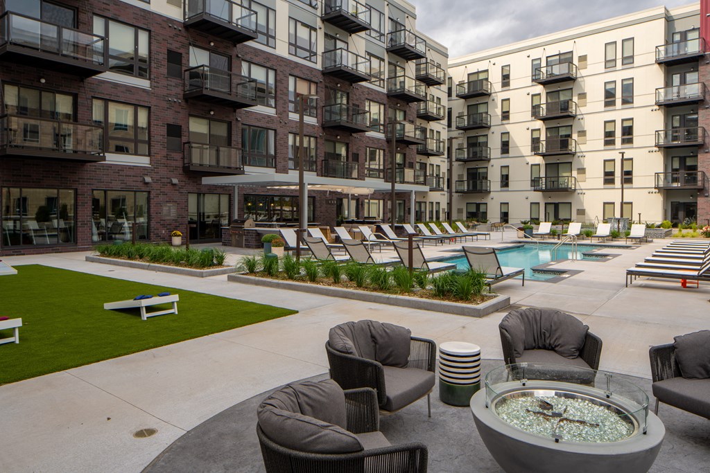 an outdoor lounge area with chairs and a fire pit in front of apartment buildings
