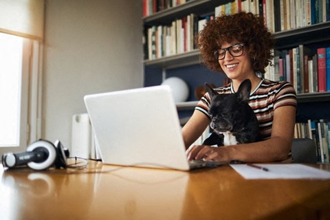 a woman sitting at a table with her dog using a laptop computer