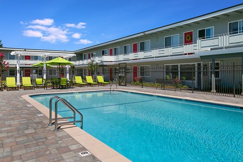 A swimming pool in front of a building with a red umbrella.