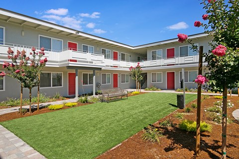 A building with red doors and windows is surrounded by a green lawn and trees.