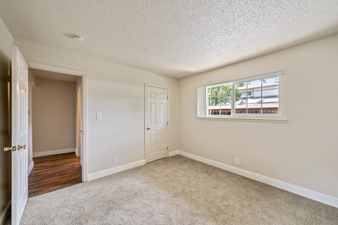 A room with a carpeted floor and a window with a view of a building outside.