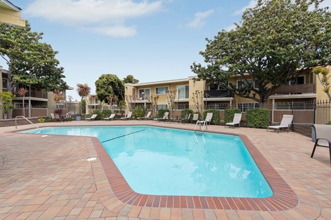 A swimming pool surrounded by a brick border and lounge chairs.