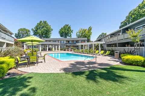 A swimming pool surrounded by a grassy area and a yellow umbrella.