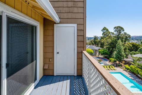 A balcony with a white door and a pool in the background.
