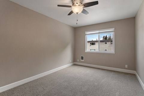 A room with a ceiling fan and a window showing a view of houses and trees outside.