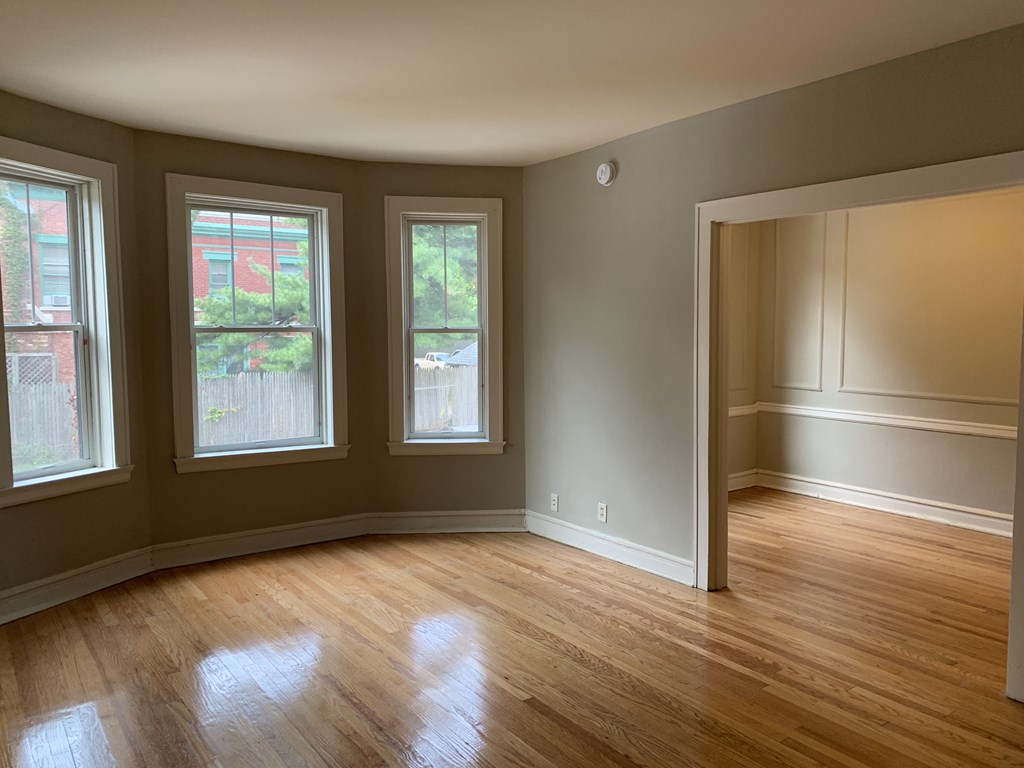 an empty living room with wooden floors and three windows