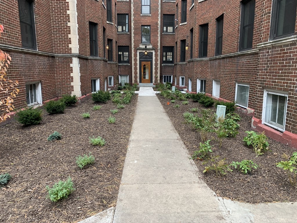 a walkway between two brick apartment buildings with a sidewalk and plants