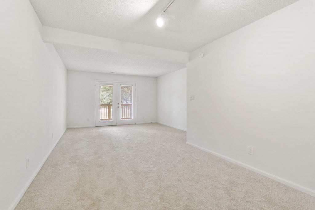 a spacious living room with white walls and carpet