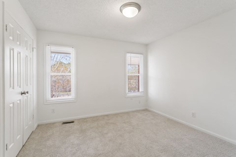 an empty bedroom with two windows and a white door