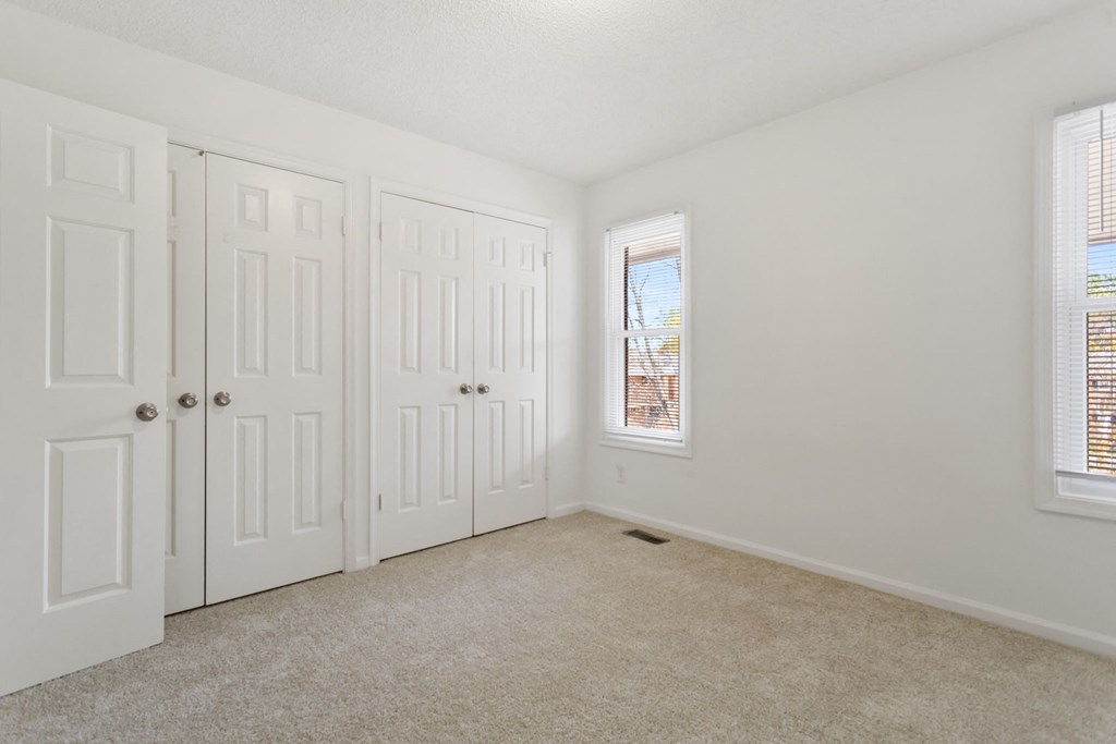 an empty bedroom with two closets and two windows