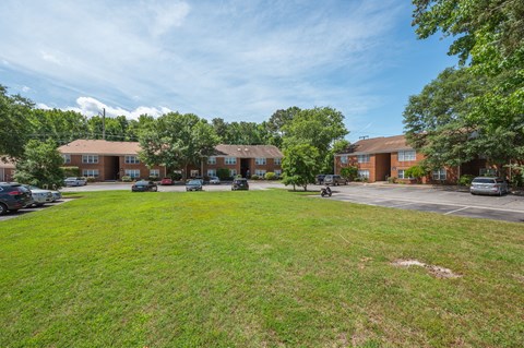 a green lawn in front of a building with cars parked in a parking lot