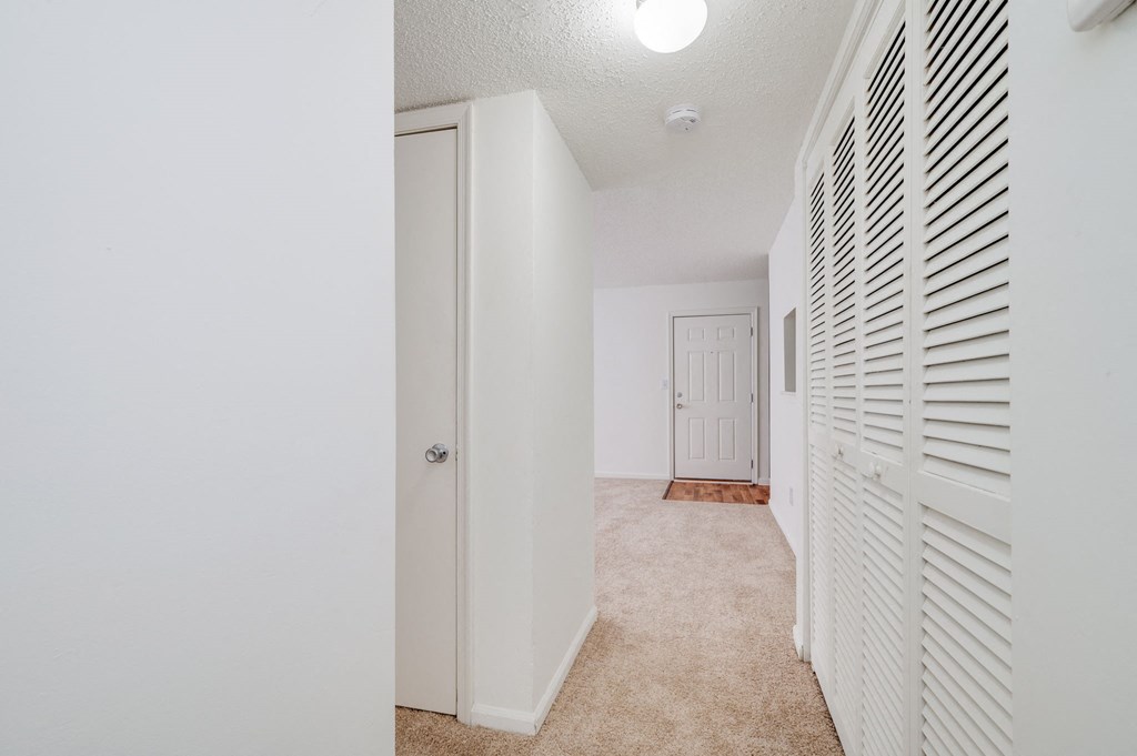 a spacious hallway with white closet doors and a door to a bedroom