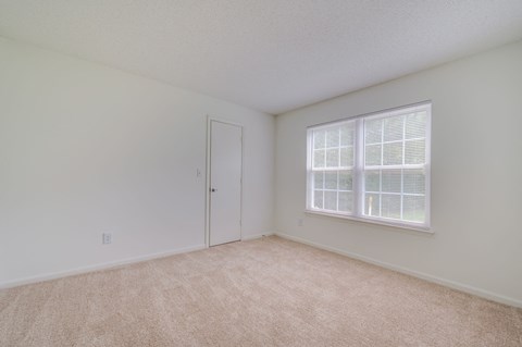 a spacious bedroom with a large window and carpeting