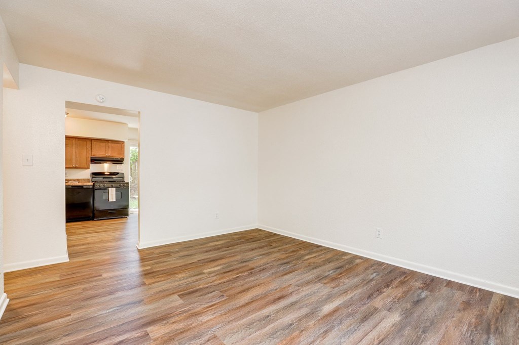 an empty living room with wood floors and a kitchen