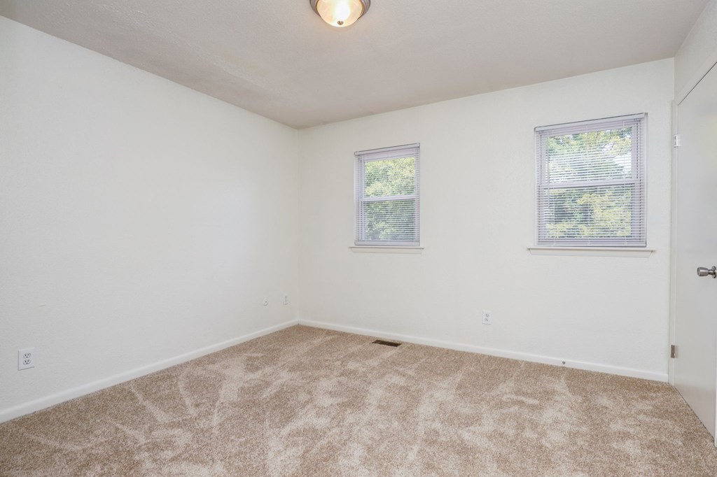 a bedroom with white walls and carpet and two windows