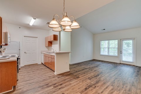 an empty living room with a kitchen and a door to the dining room