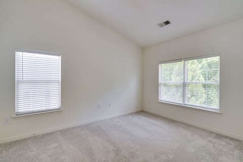 an empty bedroom with two windows and carpeting