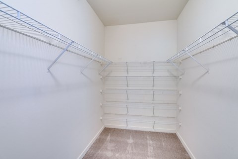 an empty closet with white walls and shelves and a beige floor