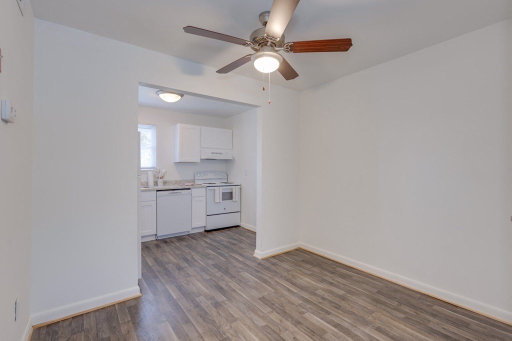 an empty living room with a ceiling fan and a kitchen