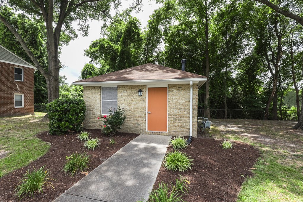 a small brick building with an orange door and a sidewalk
