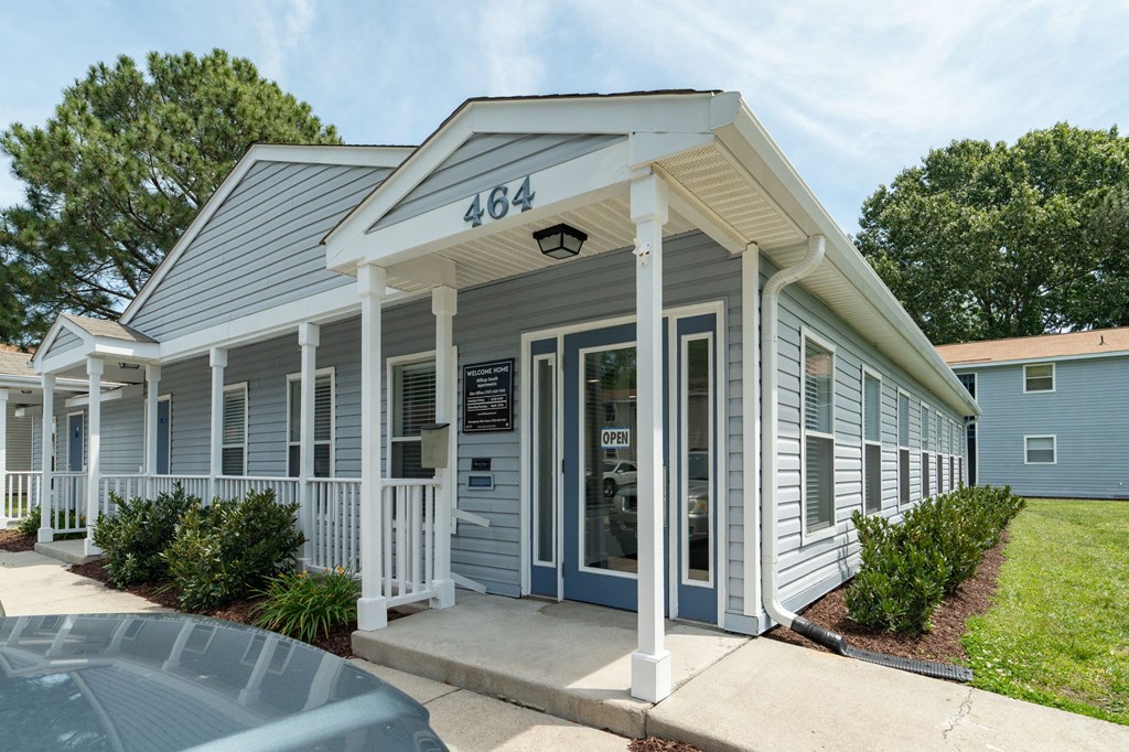 the front of a gray building with white pillars and a porch