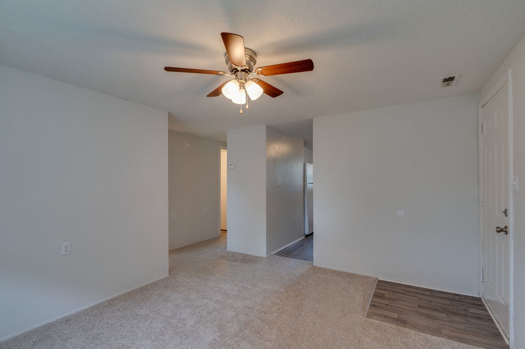an empty living room with a ceiling fan and a hallway