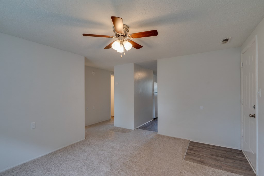an empty living room with a ceiling fan and a hallway