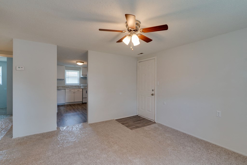 an empty living room with a ceiling fan and a kitchen