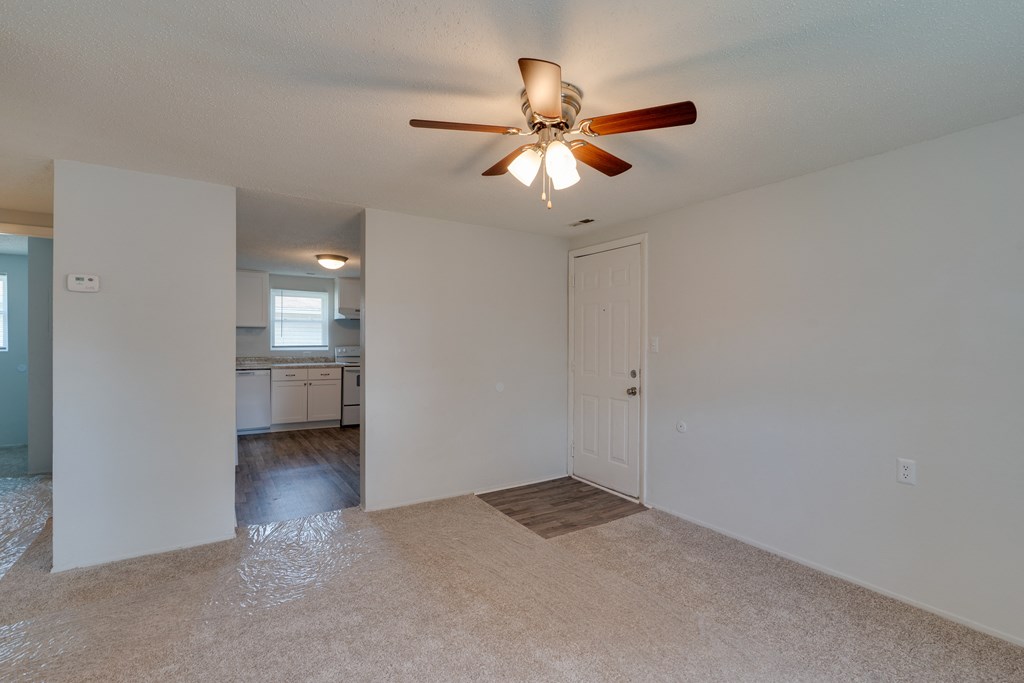 an empty living room with a ceiling fan and a kitchen