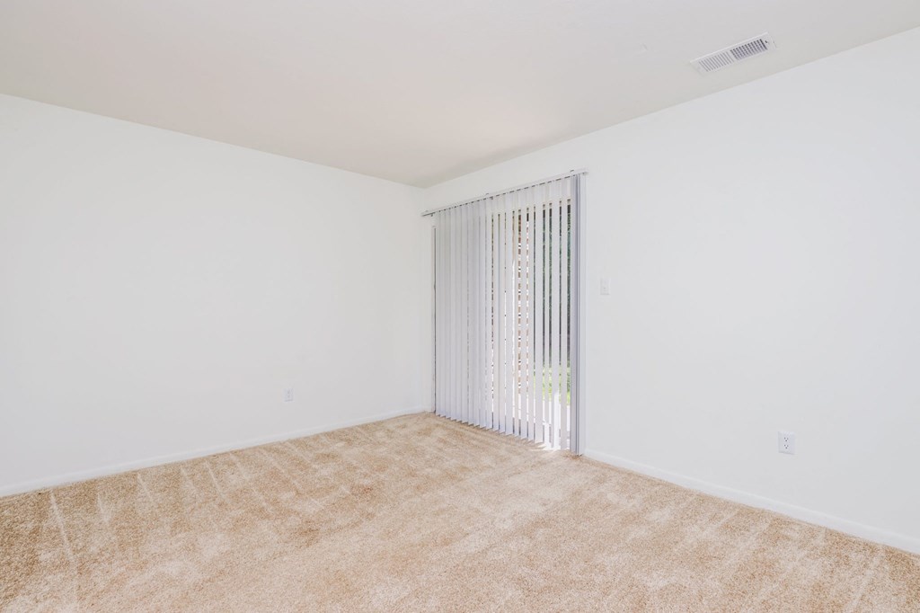 a spacious living room with white walls and a window with blinds