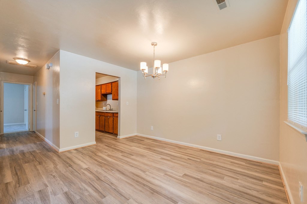 an empty living room with wood flooring and a kitchen
