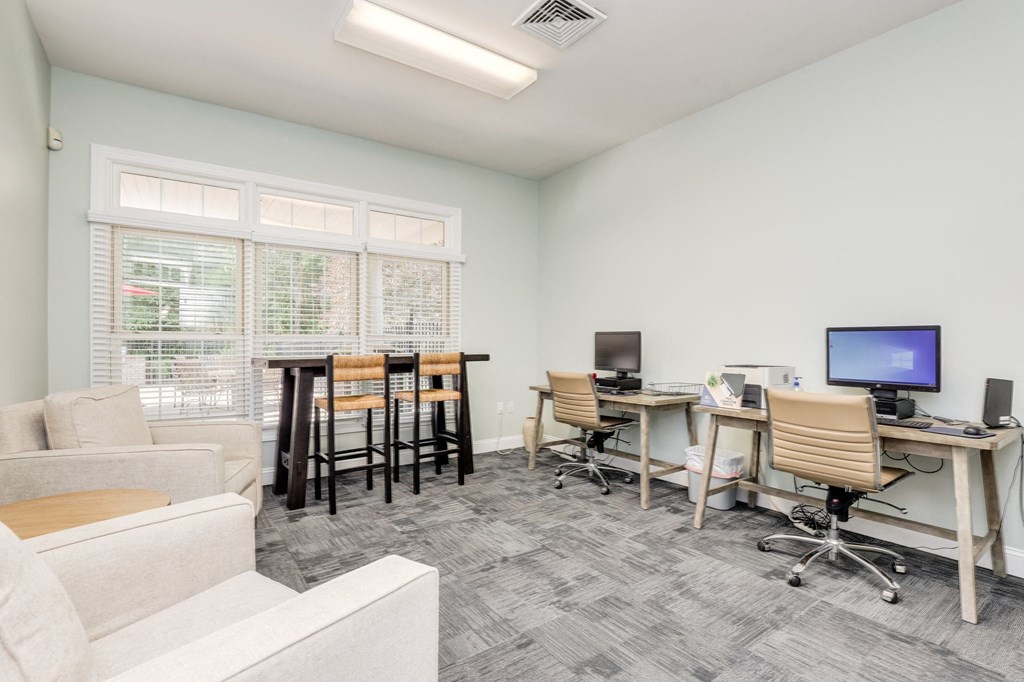 a living room with a couch and chairs and a desk with computers