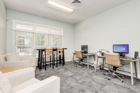 a living room with a couch and chairs and a desk with computers