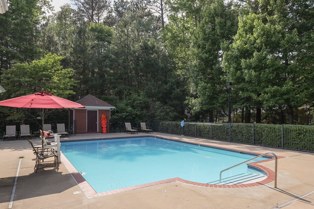 a swimming pool with a red umbrella and chairs around it